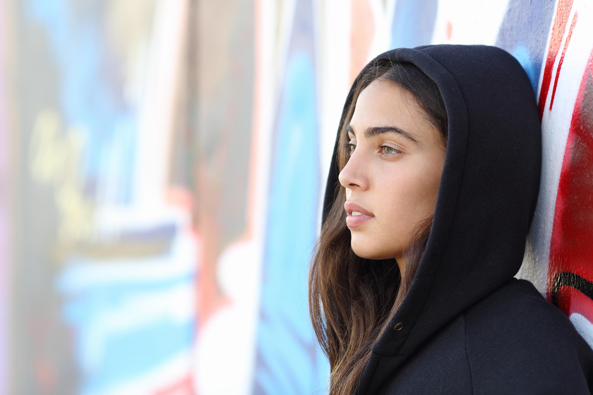 Profile portrait of a skater style teenager girl with an unfocused graffiti wall in the background