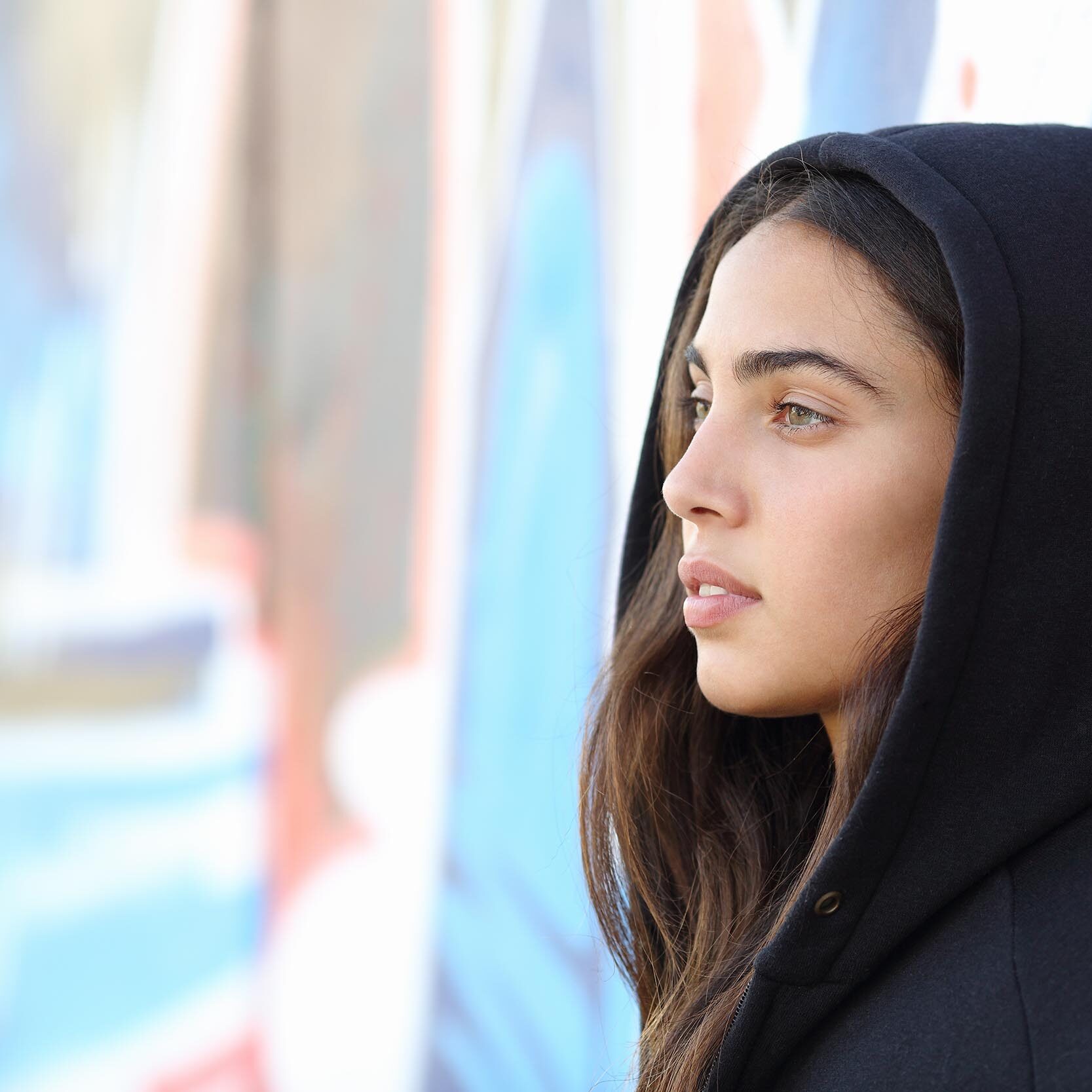 Profile portrait of a skater style teenager girl with an unfocused graffiti wall in the background