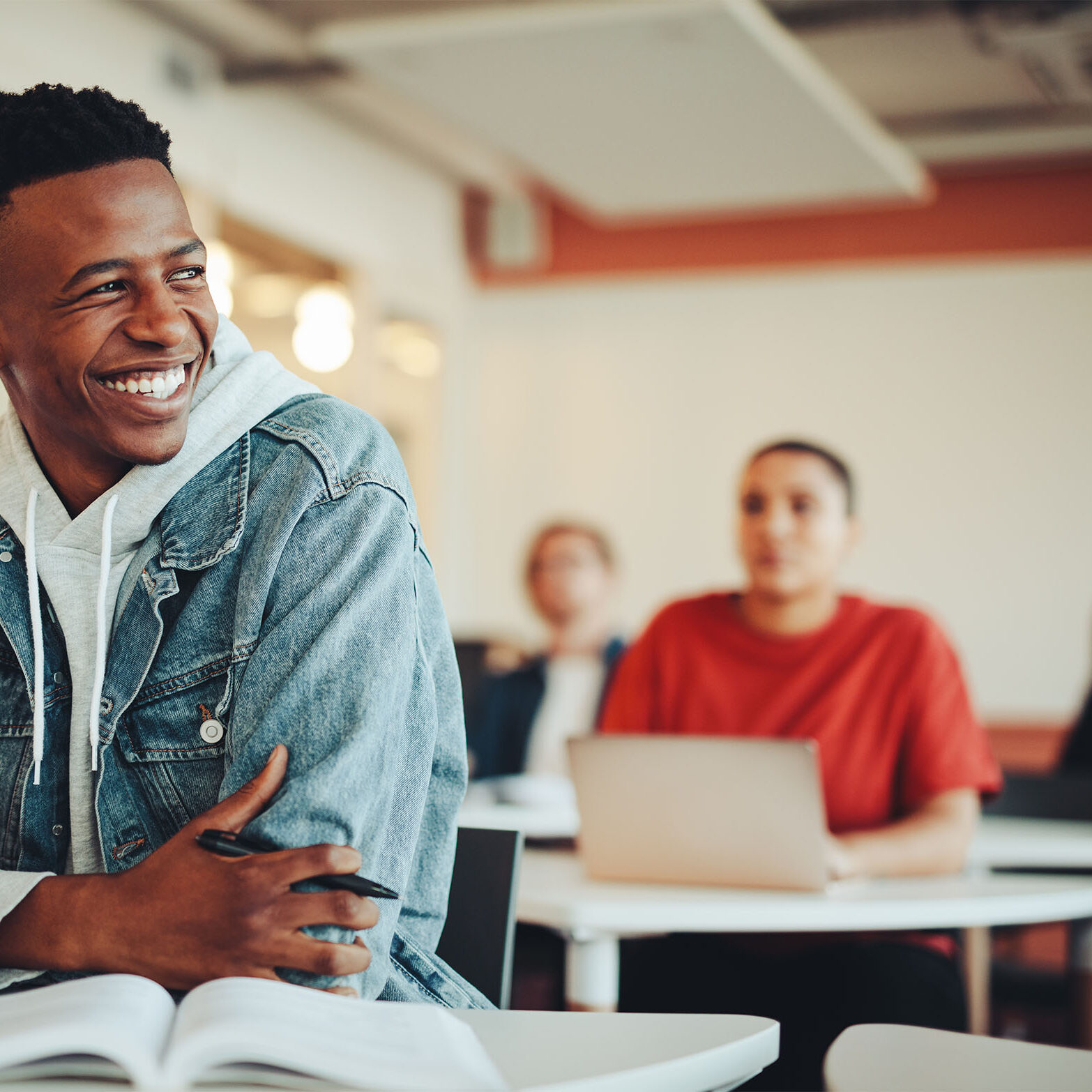 Male student sitting in university classroom looking away and smiling. Man sitting in lecture in high school classroom.